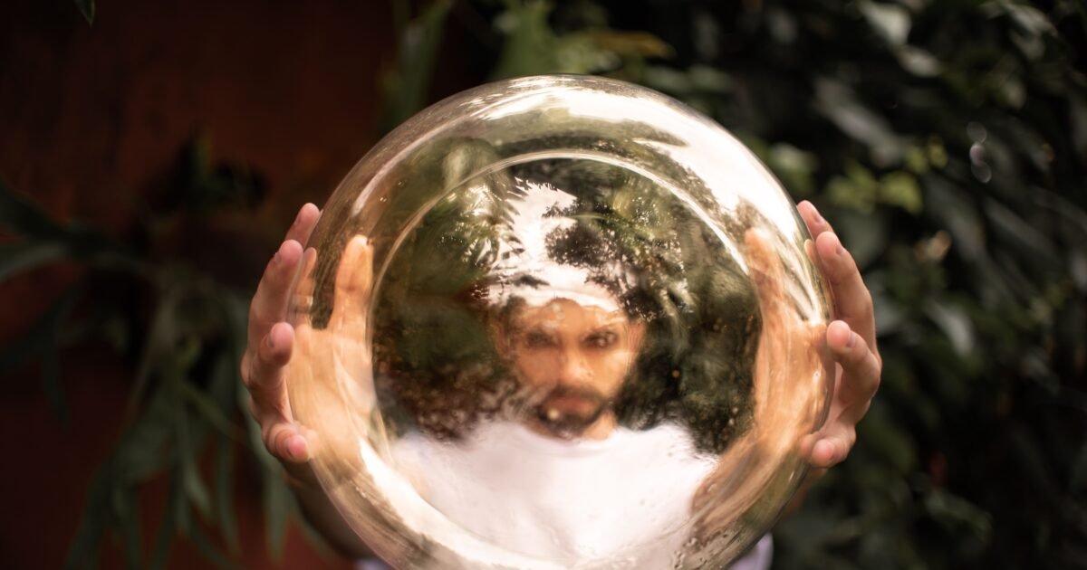 A man holds a reflective golden sphere, creating a distorted image of his face outdoors.