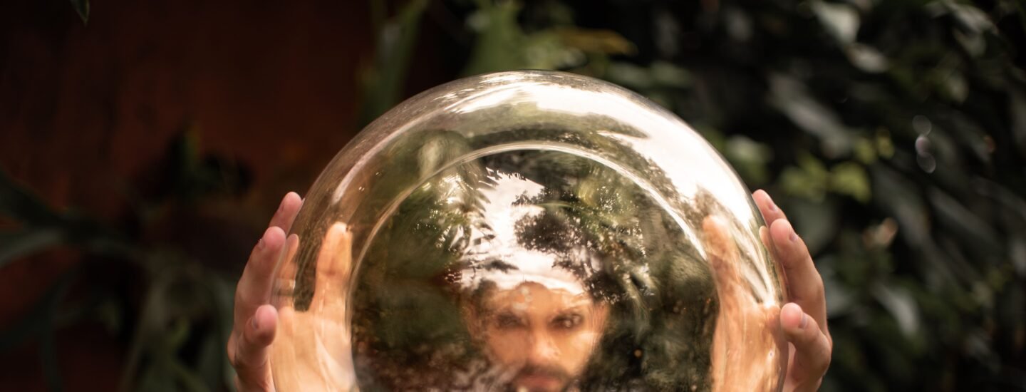 A man holds a reflective golden sphere, creating a distorted image of his face outdoors.