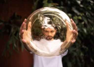 A man holds a reflective golden sphere, creating a distorted image of his face outdoors.