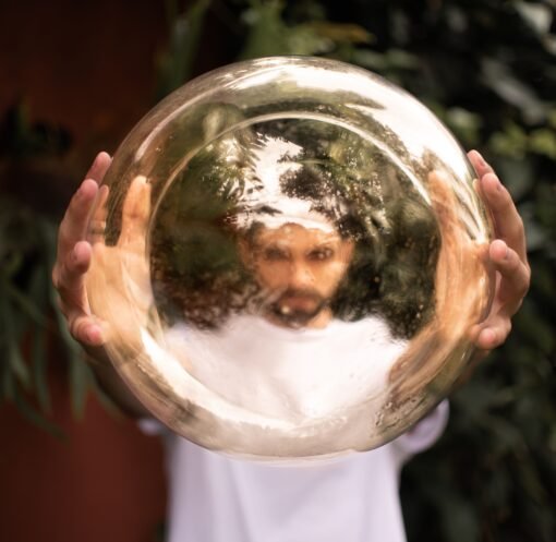 A man holds a reflective golden sphere, creating a distorted image of his face outdoors.