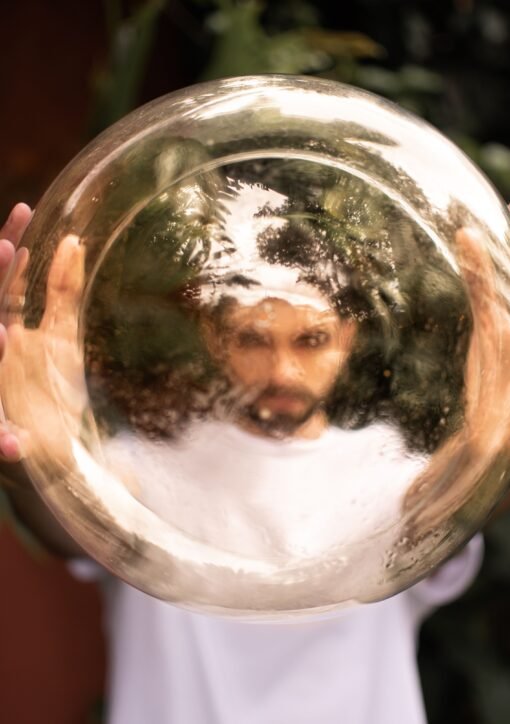 A man holds a reflective golden sphere, creating a distorted image of his face outdoors.