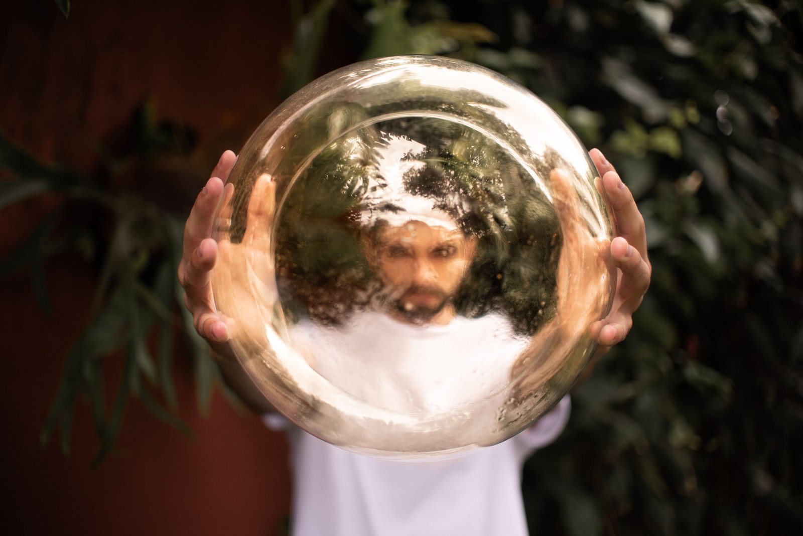 A man holds a reflective golden sphere, creating a distorted image of his face outdoors.
