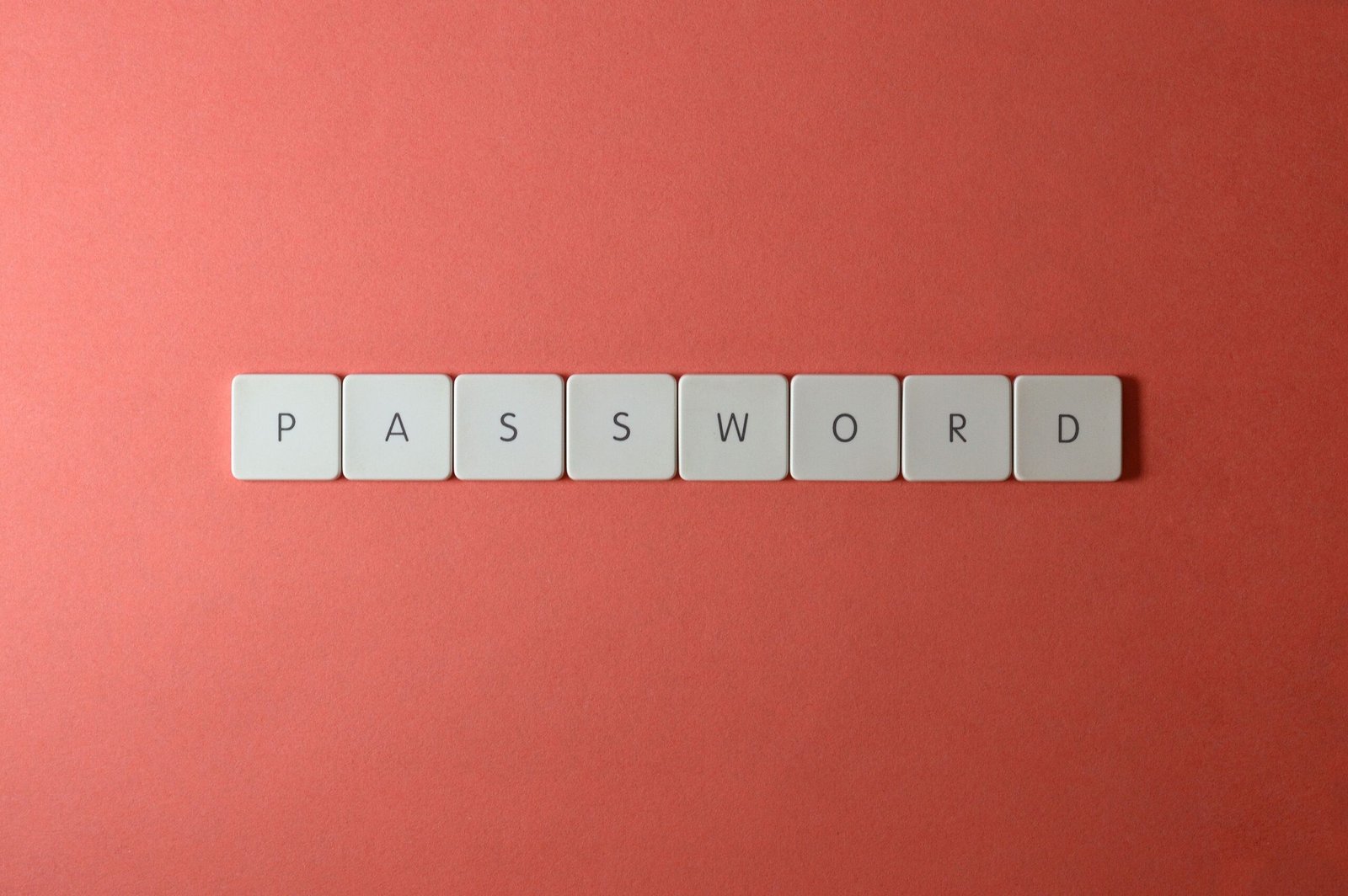 Focus on password security with white keyboard tiles spelling 'PASSWORD' on a coral background.