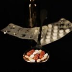 Close-up of assorted pills on a spoon with blister packs and a medicine dropper in the background.