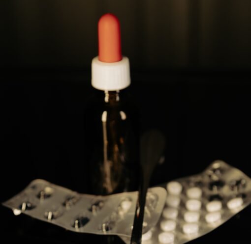 Close-up of assorted pills on a spoon with blister packs and a medicine dropper in the background.