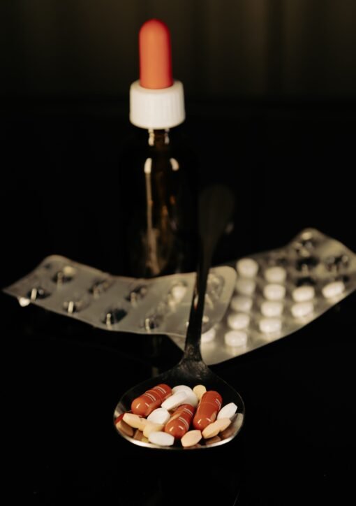 Close-up of assorted pills on a spoon with blister packs and a medicine dropper in the background.