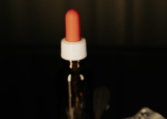 Close-up of assorted pills on a spoon with blister packs and a medicine dropper in the background.