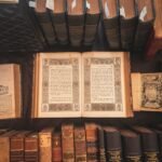 A collection of vintage books displayed in an antique library setting with an open ornate book highlighted.