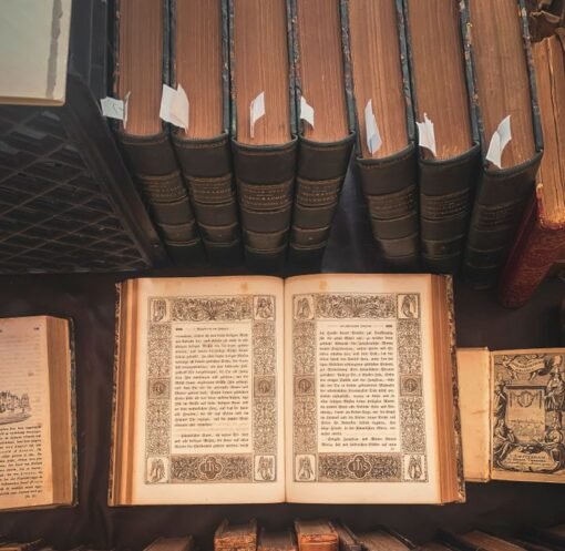 A collection of vintage books displayed in an antique library setting with an open ornate book highlighted.