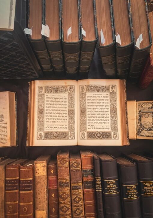 A collection of vintage books displayed in an antique library setting with an open ornate book highlighted.