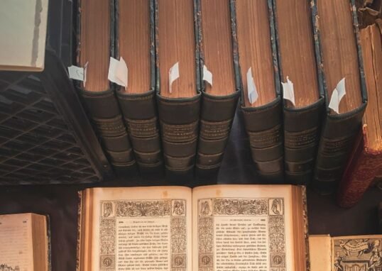 A collection of vintage books displayed in an antique library setting with an open ornate book highlighted.
