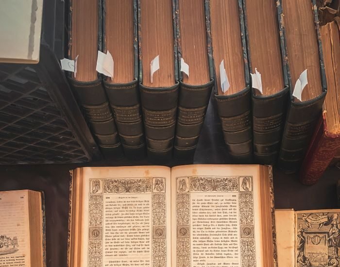 A collection of vintage books displayed in an antique library setting with an open ornate book highlighted.