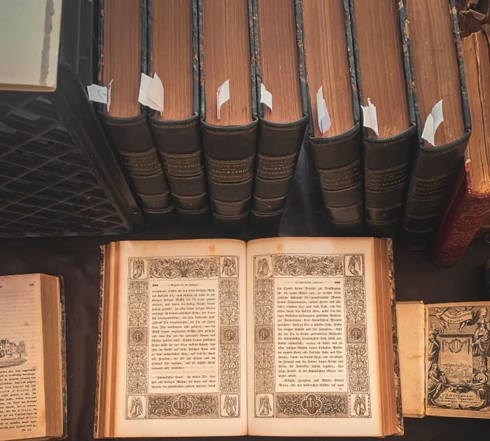 A collection of vintage books displayed in an antique library setting with an open ornate book highlighted.