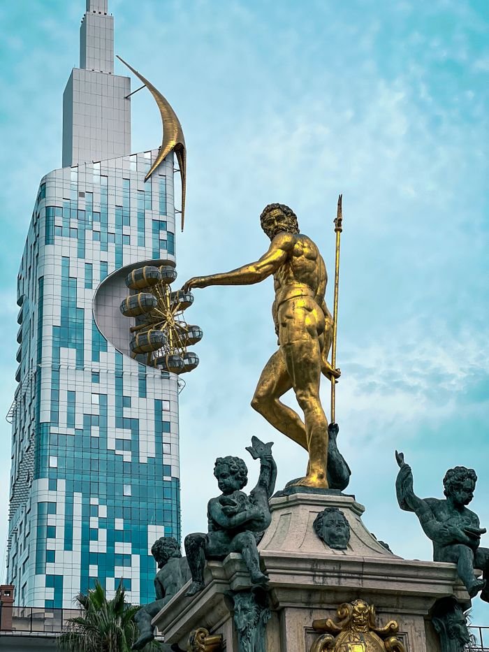 Iconic golden statue with modern skyscraper in Batumi, Georgia's vibrant cityscape.