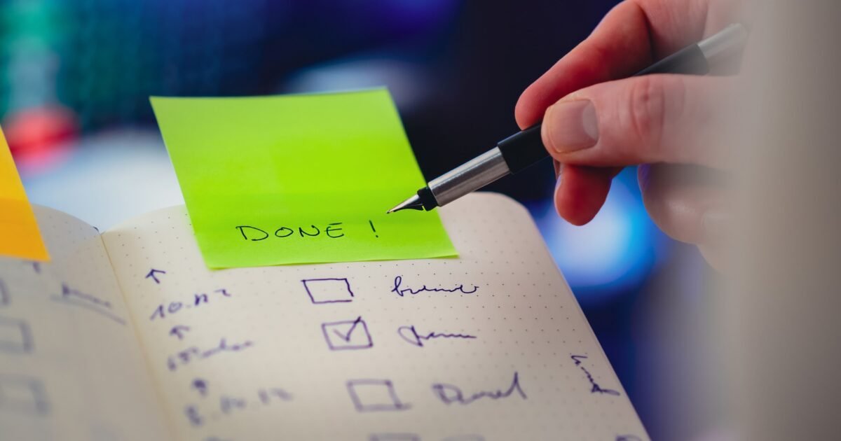 Close-up of a checklist and pen with brightly colored sticky note that says 'DONE!' indicating task completion.