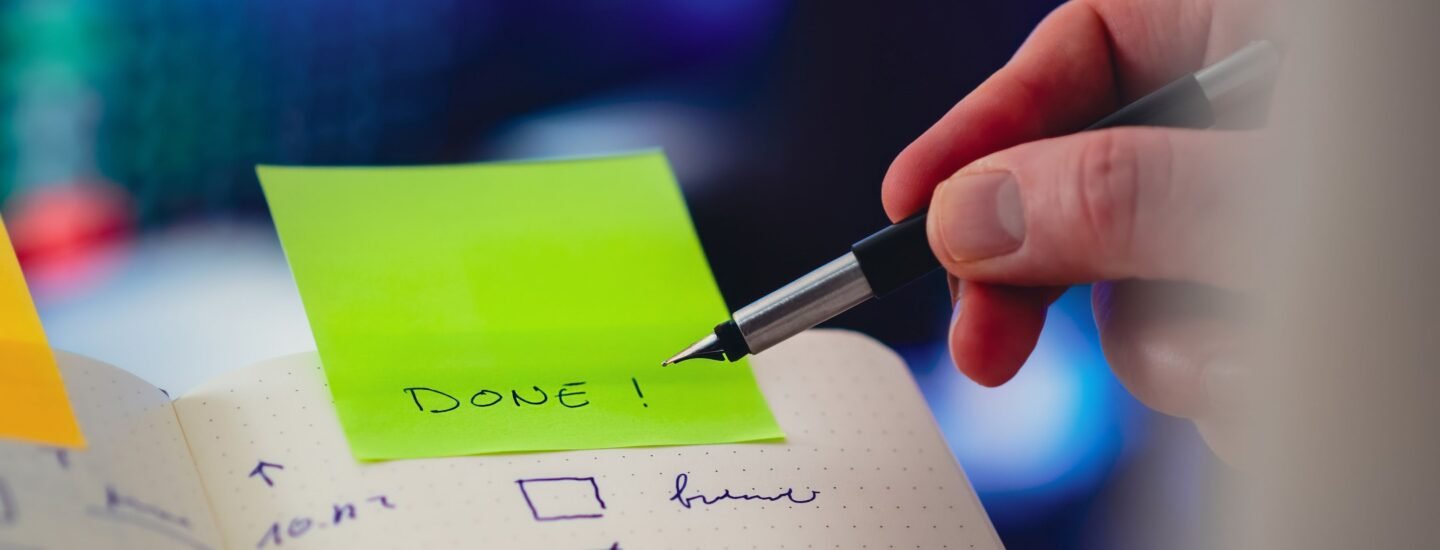Close-up of a checklist and pen with brightly colored sticky note that says 'DONE!' indicating task completion.