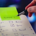 Close-up of a checklist and pen with brightly colored sticky note that says 'DONE!' indicating task completion.