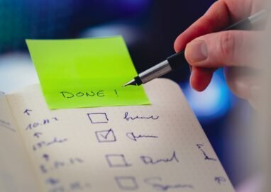 Close-up of a checklist and pen with brightly colored sticky note that says 'DONE!' indicating task completion.