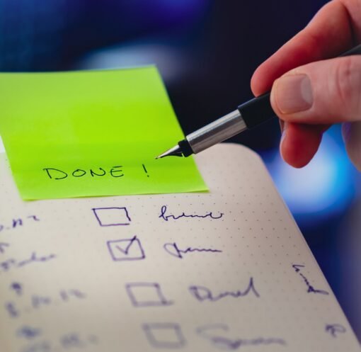 Close-up of a checklist and pen with brightly colored sticky note that says 'DONE!' indicating task completion.