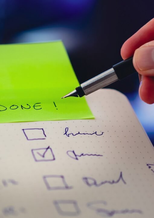 Close-up of a checklist and pen with brightly colored sticky note that says 'DONE!' indicating task completion.