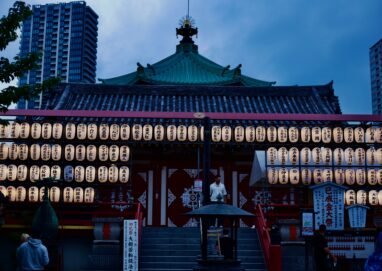 A serene view of a Japanese temple adorned with lanterns during twilight.