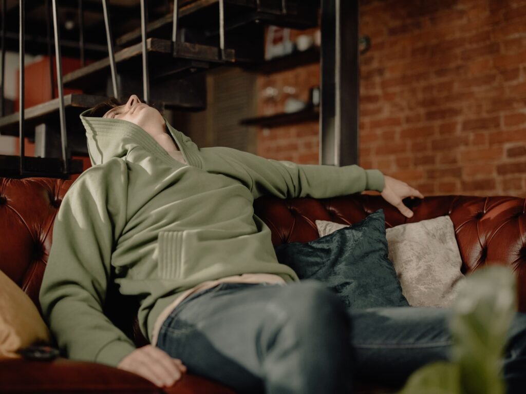 A young man in a green hoodie relaxes on a leather sofa at home, embodying a cozy and laid-back atmosphere.