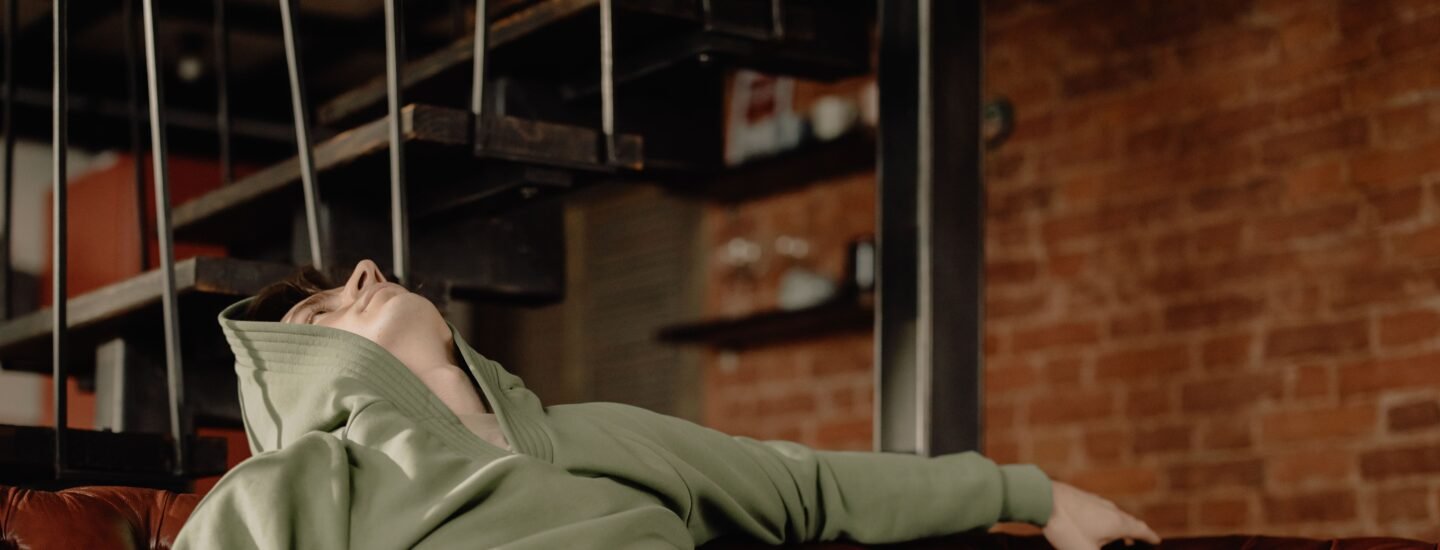 A young man in a green hoodie relaxes on a leather sofa at home, embodying a cozy and laid-back atmosphere.