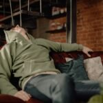 A young man in a green hoodie relaxes on a leather sofa at home, embodying a cozy and laid-back atmosphere.