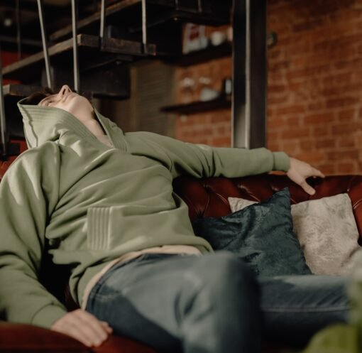 A young man in a green hoodie relaxes on a leather sofa at home, embodying a cozy and laid-back atmosphere.