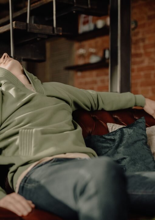 A young man in a green hoodie relaxes on a leather sofa at home, embodying a cozy and laid-back atmosphere.
