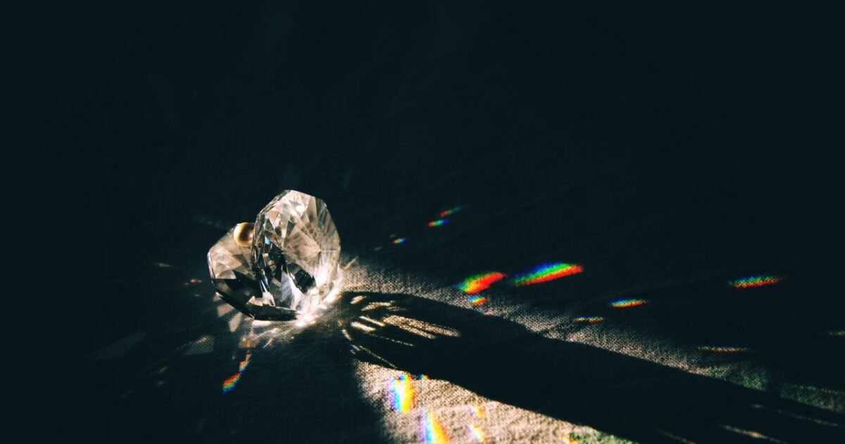 A diamond-shaped crystal casting rainbow reflections on a surface with dramatic lighting.