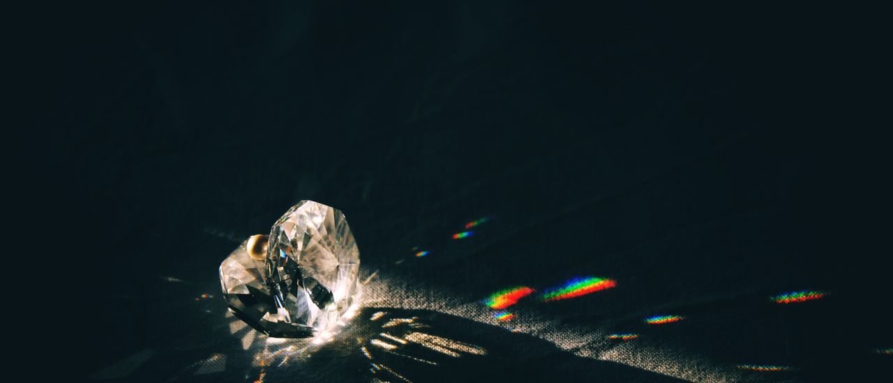 A diamond-shaped crystal casting rainbow reflections on a surface with dramatic lighting.