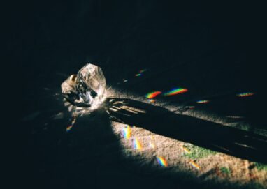 A diamond-shaped crystal casting rainbow reflections on a surface with dramatic lighting.