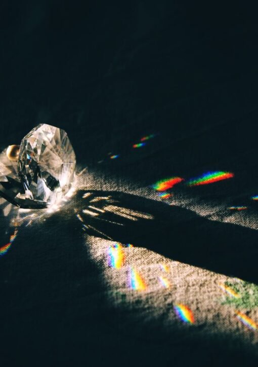 A diamond-shaped crystal casting rainbow reflections on a surface with dramatic lighting.