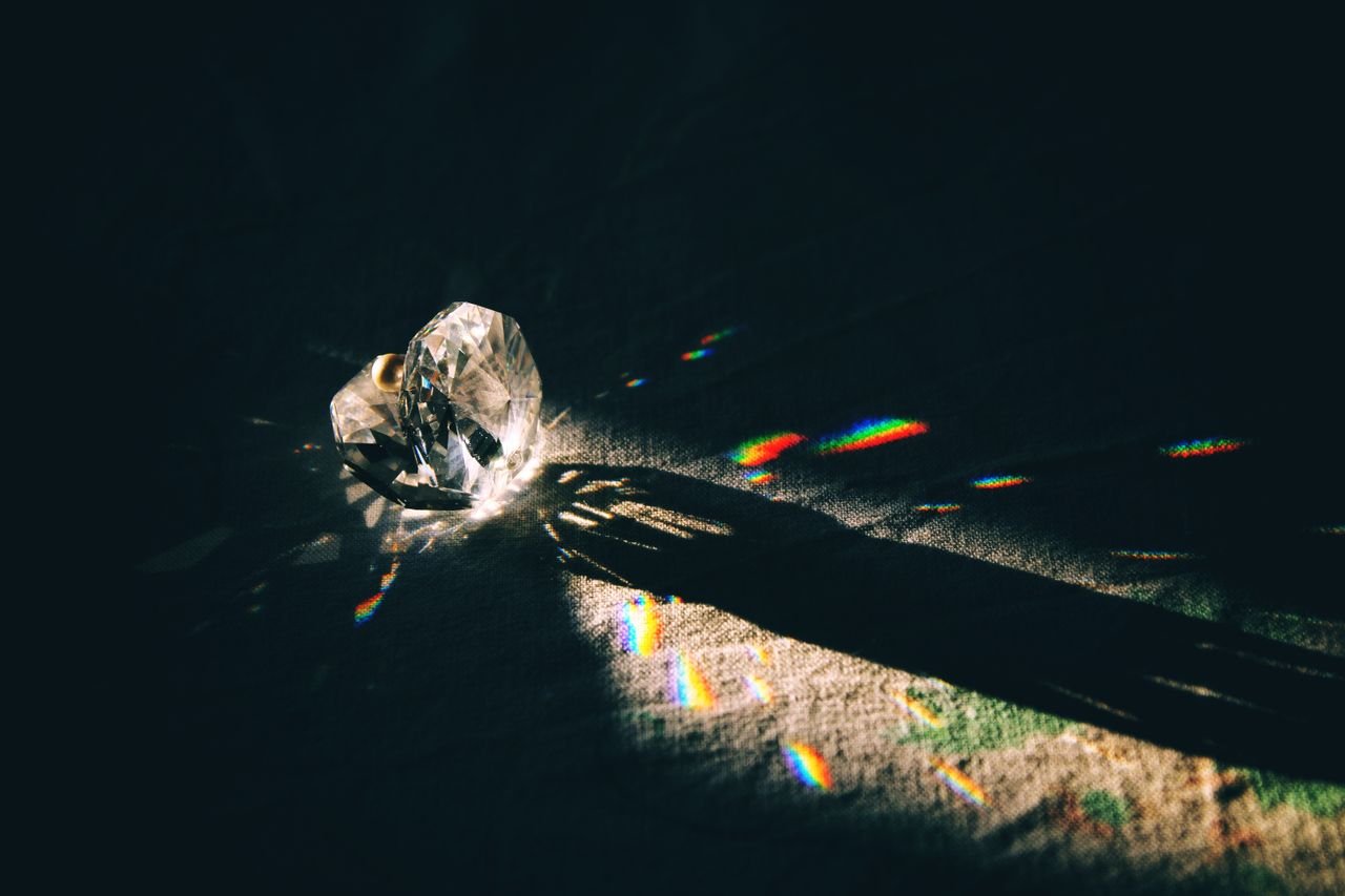 A diamond-shaped crystal casting rainbow reflections on a surface with dramatic lighting.