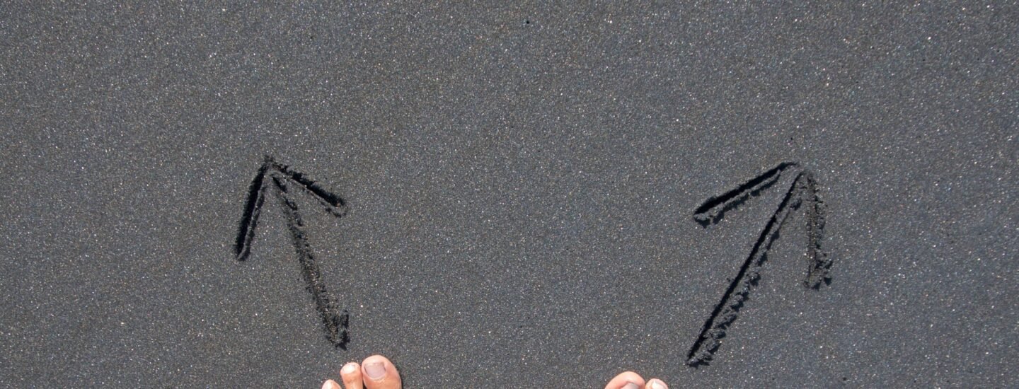 A pair of bare feet on Bali's beach sand with arrows drawn, symbolizing choice and direction.