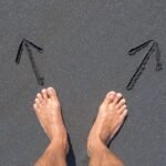 A pair of bare feet on Bali's beach sand with arrows drawn, symbolizing choice and direction.