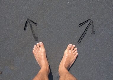 A pair of bare feet on Bali's beach sand with arrows drawn, symbolizing choice and direction.