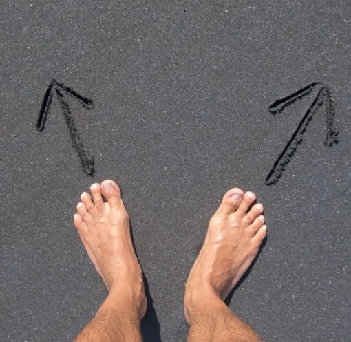 A pair of bare feet on Bali's beach sand with arrows drawn, symbolizing choice and direction.
