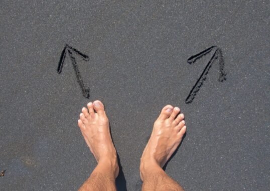 A pair of bare feet on Bali's beach sand with arrows drawn, symbolizing choice and direction.