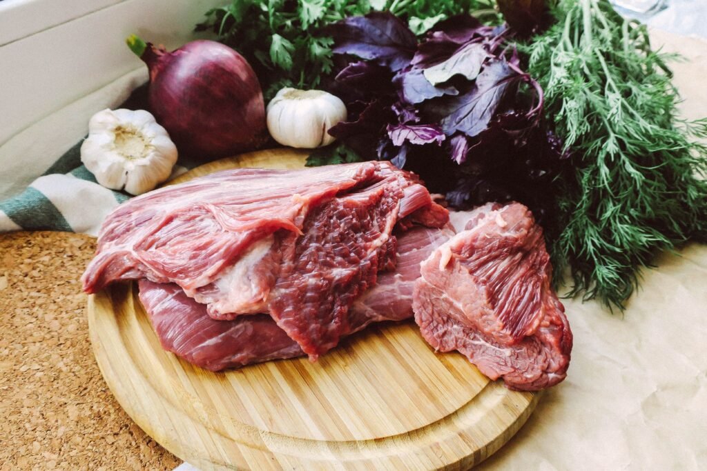 Close-up of raw beef on a wooden board with fresh herbs and vegetables.