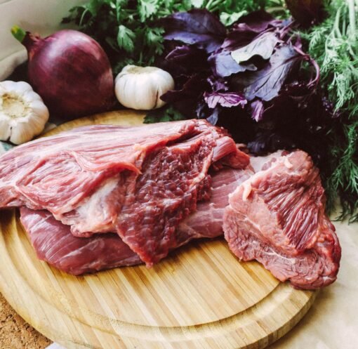Close-up of raw beef on a wooden board with fresh herbs and vegetables.