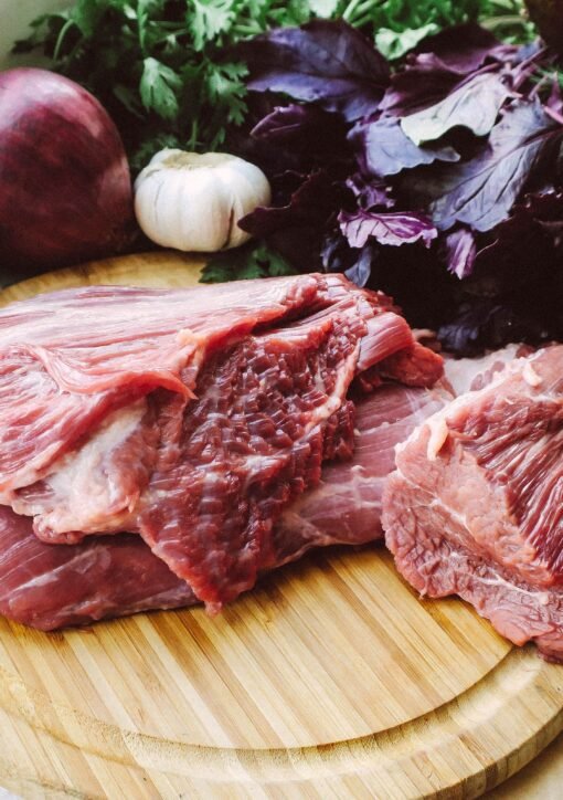 Close-up of raw beef on a wooden board with fresh herbs and vegetables.