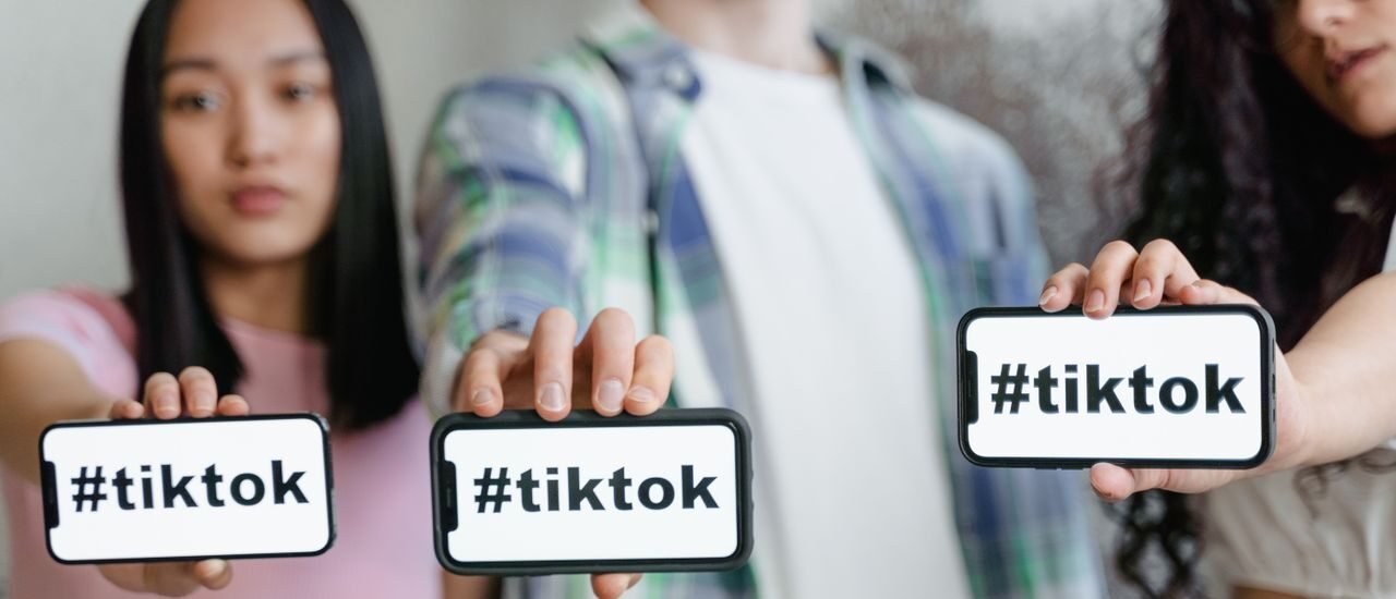 Young adults holding smartphones with TikTok hashtag, showcasing social media engagement.