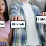 Young adults holding smartphones with TikTok hashtag, showcasing social media engagement.