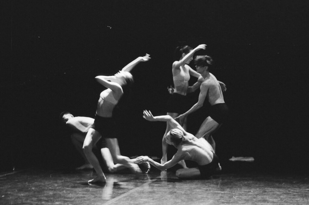 Artistic black and white photo of a group of ballet dancers in motion on stage.