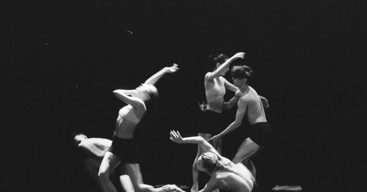 Artistic black and white photo of a group of ballet dancers in motion on stage.
