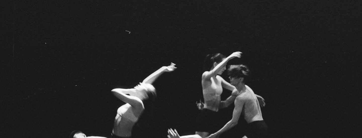 Artistic black and white photo of a group of ballet dancers in motion on stage.