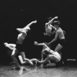 Artistic black and white photo of a group of ballet dancers in motion on stage.
