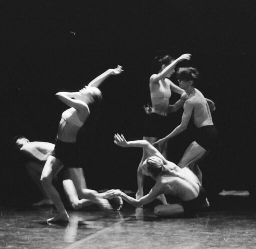 Artistic black and white photo of a group of ballet dancers in motion on stage.